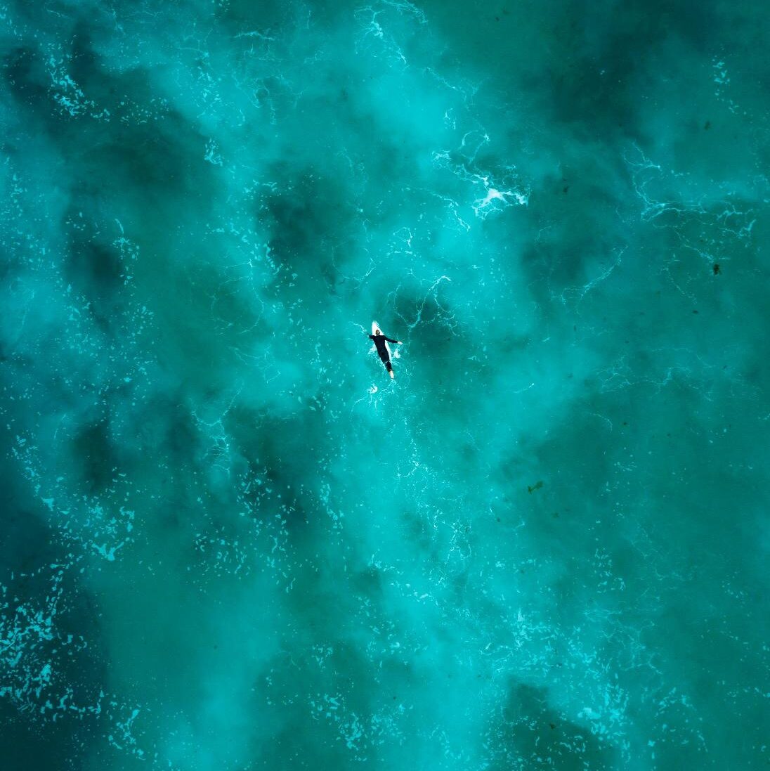 a sky view of a surfer in the middle of the ocean